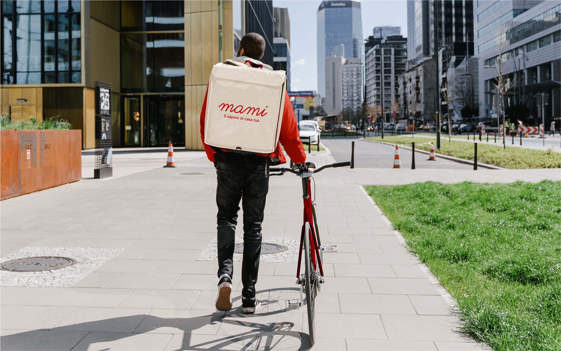 Foto di un rider Mami con borsa contenente il cibo da consegnare e bicicletta personalizzati con la visual identity di Mami